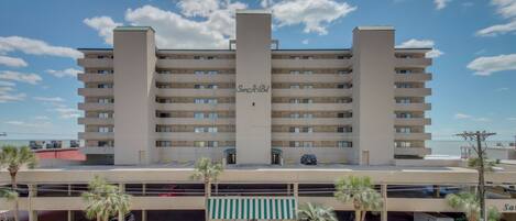 A multi-story hotel with a central atrium, parking garage, and a beach view.