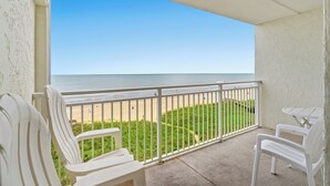 A balcony with white chairs and a table, overlooking a beach with a clear sky. - Oceanfront Condo with indoor pool + Free Attraction Tickets! (North Myrtle Beach)