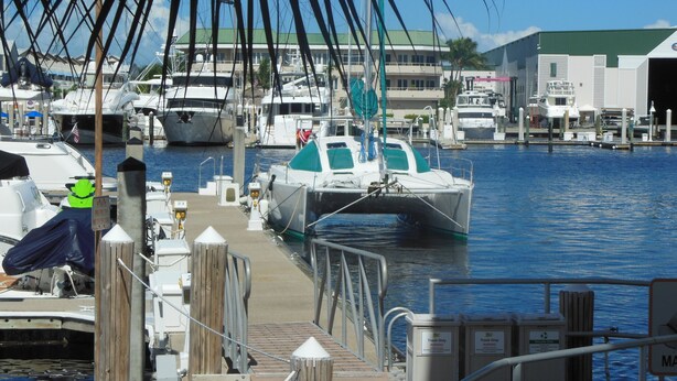A marina with boats docked, a wooden dock, and a building in the background. - Sailing catamaran vacation rentals in Pensacola Beach (Pensacola Beach)