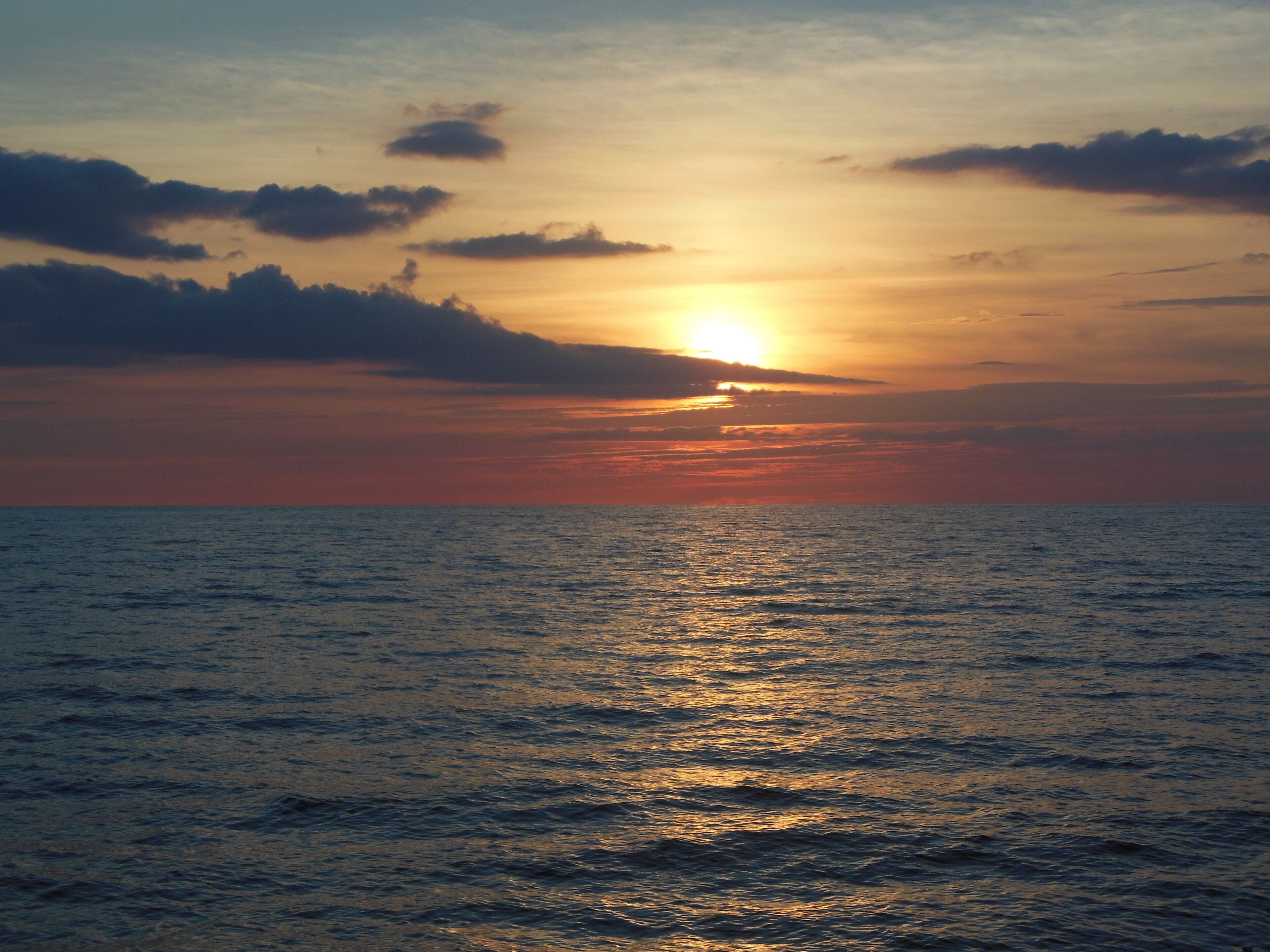A sunset over a calm sea with clouds in the sky.