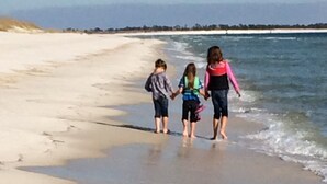A beach with three people walking along the shoreline. - Sailing catamaran vacation rentals in Pensacola Beach (Pensacola Beach)