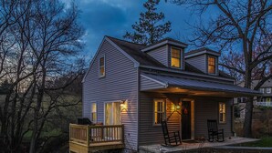 Une maison à deux étages dotée d’un porche couvert, d’une petite terrasse et d’une porte d’entrée avec un luminaire.