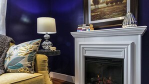 Une pièce avec une cheminée blanche, un mur bleu, une lampe et un canapé agrémenté de coussins décoratifs.