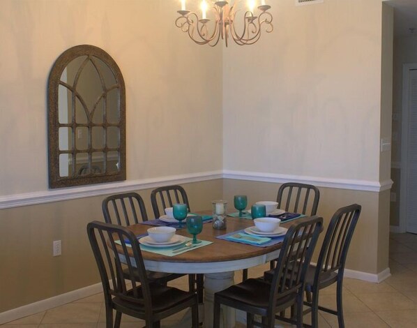 A dining area with a round table, six chairs, and a chandelier.