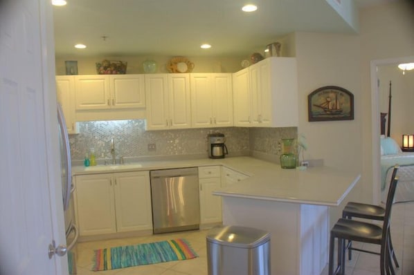 A kitchen with white cabinets, a dishwasher, a coffee maker, and a small island with two chairs.