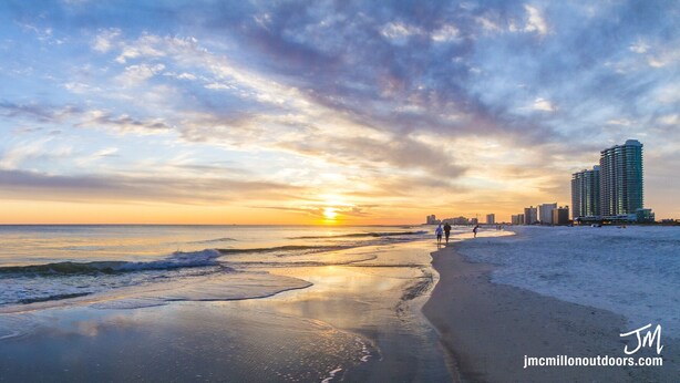 Een strand met een zonsondergang, golven en een stadsachtergrond.