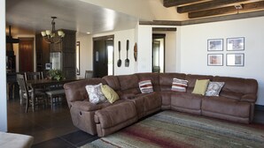 A spacious living room with a brown sectional sofa, a dining area with wooden chairs, and a kitchen in the background. - Spectacular Home Near Zion with Pool and Hot Tub (Virgin)