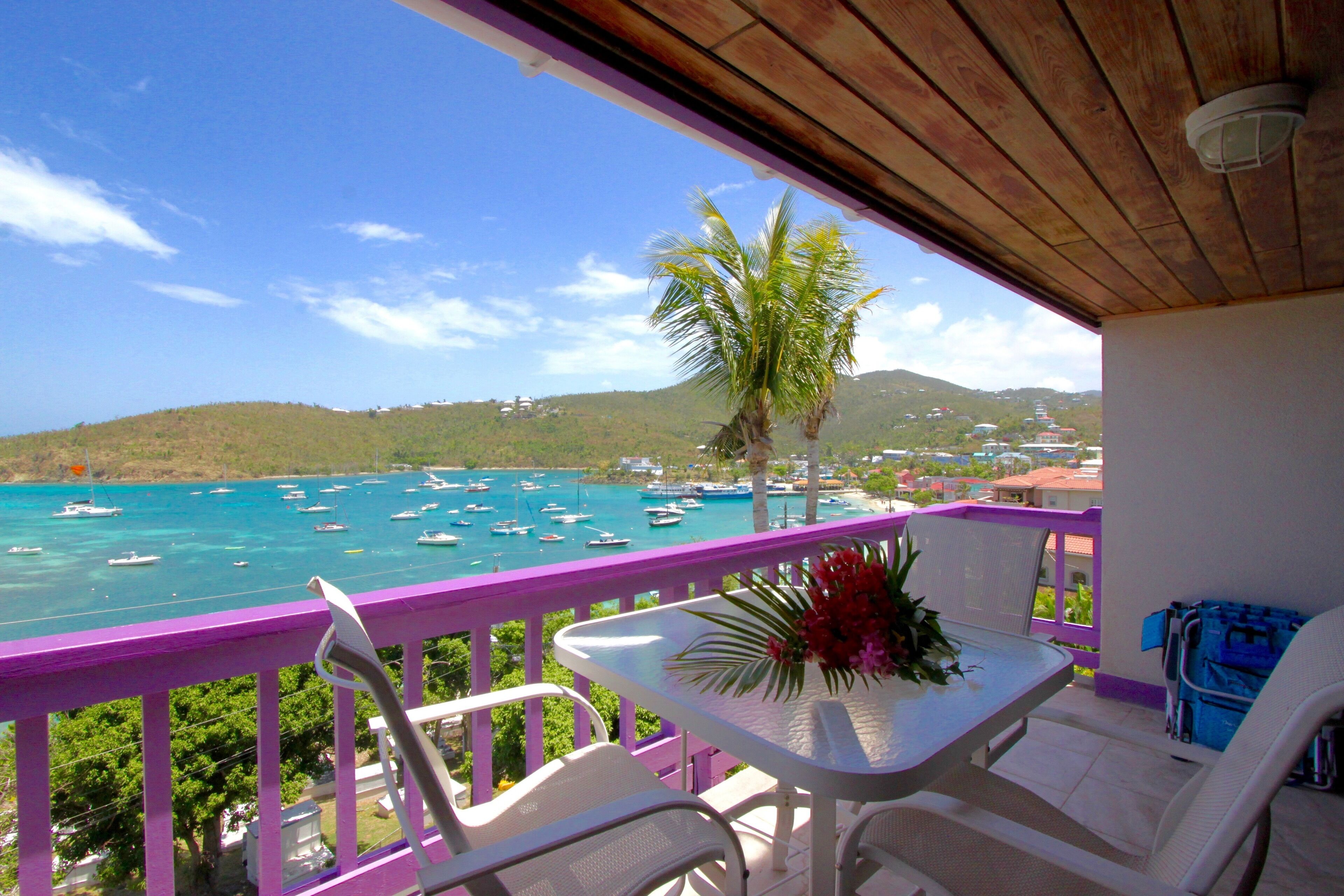 A balcony with a view of the sea, a table with chairs, and a flower vase.