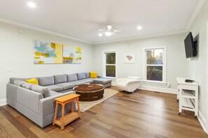 Uma sala de estar moderna com um sofá seccional, um banquinho redondo, uma poltrona branca e uma pequena mesa de madeira.