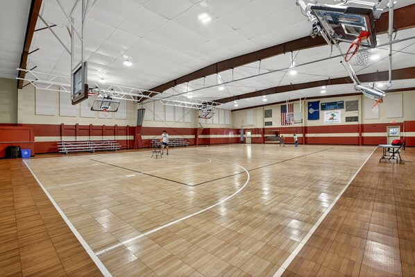 An indoor basketball court with a wooden floor, basketball hoops, and bleachers. - One Block to Beach! Modern 6 Bed with Private Pool (Isle Of Palms)