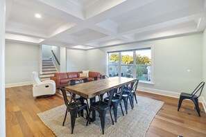 Uma área de refeições espaçosa com mesa de madeira e cadeiras pretas, um sofá de couro e uma escada que dá para outro andar.