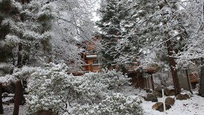 A snowy landscape with a wooden cabin and a large rock formation. - 30 night minimum stay, Log Style Cabin in Moonridge, Walk To Slopes, Ntl. Forest (Big Bear Lake)