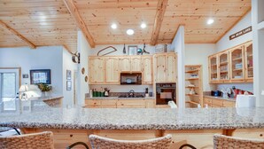 A spacious kitchen with wooden cabinets, granite countertops, and a central island with chairs. - 30 night minimum stay, Log Style Cabin in Moonridge, Walk To Slopes, Ntl. Forest (Big Bear Lake)