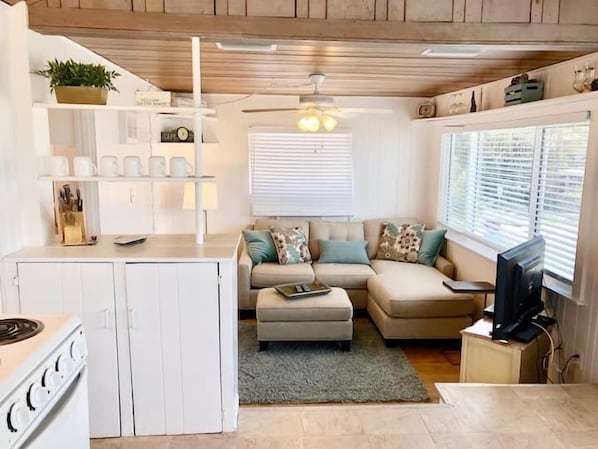 A compact living space with a kitchenette, a sofa set, a ceiling fan, and a TV.