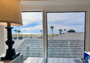 A room with a view of a beach, a lamp, and a window with a view of palm trees and a stop sign. - Pass-a-Grille Gulf Front Cottage, Ocean View (St Pete Beach)