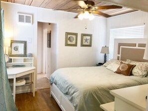 Une chambre à coucher comprenant un lit, un bureau, un ventilateur de plafond et des éléments décoratifs sur les murs.