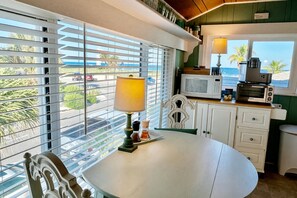 A kitchen with a view of the beach, a table with a lamp, and a microwave on the counter. - Pass-a-Grille Gulf Front Cottage, Ocean View (St Pete Beach)