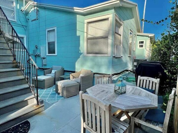 Une maison bleue avec un patio couvert, du mobilier d’extérieur et un escalier.