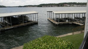 Two docked boats with covered decks, a grassy area in the foreground, and a distant shoreline with buildings. - Off Season Rates!  Ideal location on Lake Hamilton! (Lake Hamilton)