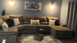 A modern living room with a sectional sofa, a small side table, and a decorative wall piece. - Off Season Rates!  Ideal location on Lake Hamilton! (Lake Hamilton)