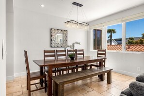 Un comedor con mesa de madera, sillas, un banco, candelabro, espejo y planta en maceta.