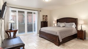 A bedroom with a large bed, a TV mounted on the wall, a small table, and a chair.