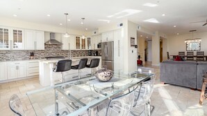 A modern kitchen with white cabinets, a stone backsplash, and a central island with chairs. - Luxurious Ocean 4bd/3ba Oceanview Villa (Santa Cruz)