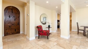 A spacious hallway with a wooden door, a red upholstered chair, a small table with a plant, and a round mirror on the wall. - Luxurious Ocean 4bd/3ba Oceanview Villa (Santa Cruz)