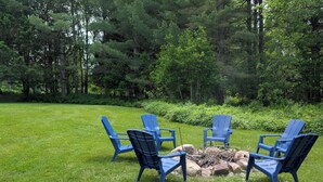 Ein grünes Freigelände mit vier blauen Adirondack-Stühlen, die um eine kleine Feuerstelle angeordnet sind.