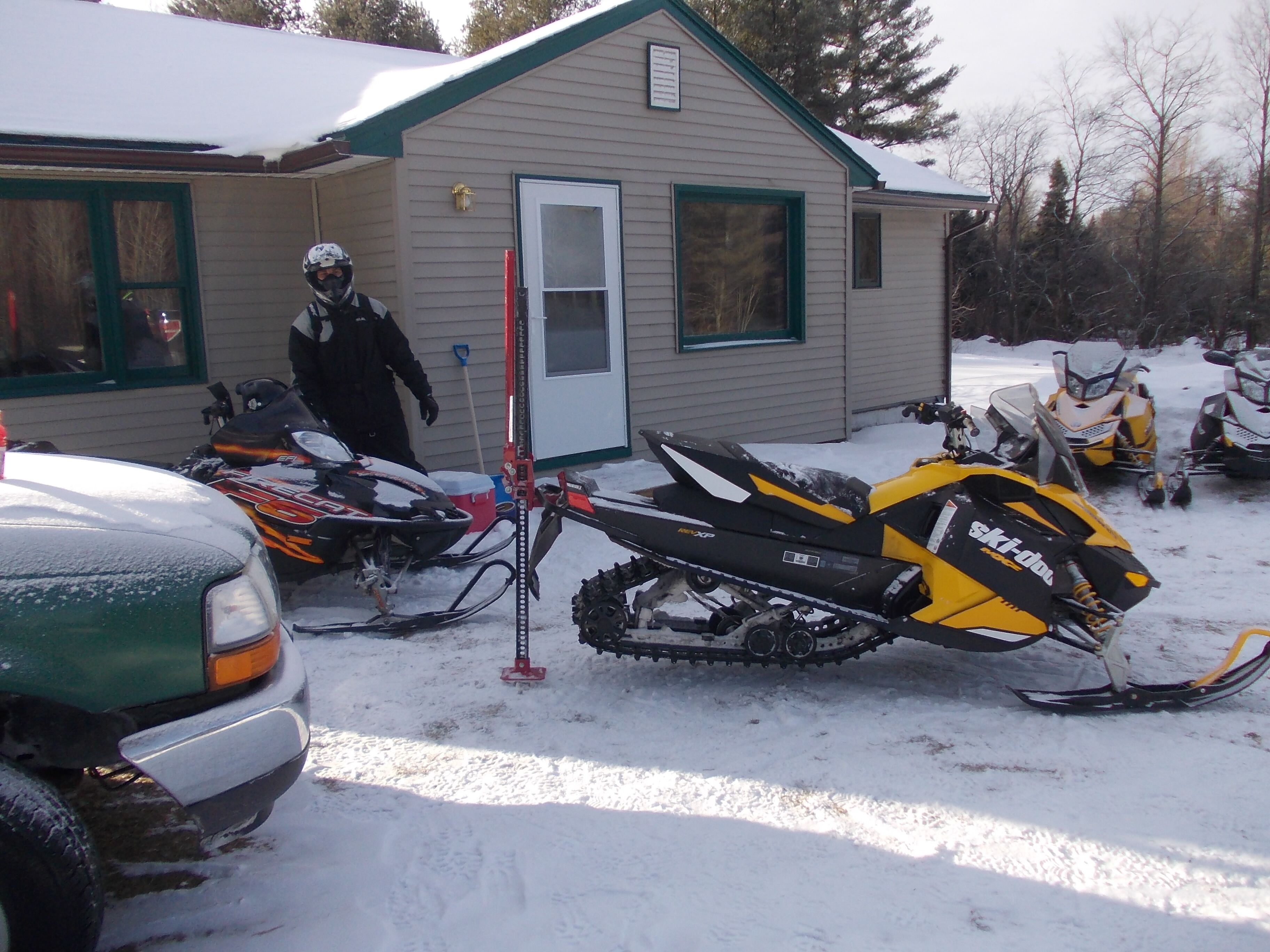Una moto de nieve estacionada frente a un edificio con puerta y ventanas, y otra moto de nieve al fondo.