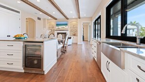 Une cuisine spacieuse avec des poutres en bois, un grand îlot central et une vue sur l’océan par les fenêtres.