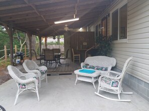 A covered patio with wicker furniture, a table, and chairs. - Turtle Time - 4 Bd House Near Holden Beach - escape the crowds! (Supply)