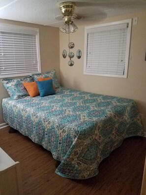 A bedroom with a patterned bedspread, two pillows, a ceiling fan, and two windows with blinds. - Turtle Time - 4 Bd House Near Holden Beach - escape the crowds! (Supply)