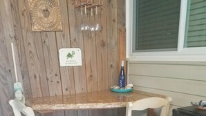 A wooden dining table with two white chairs, a small black cabinet, and a window with blinds. - Turtle Time - 4 Bd House Near Holden Beach - escape the crowds! (Supply)