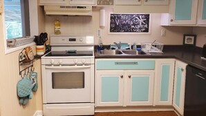 A kitchen with white and teal cabinets, a stove, a sink, and a chalkboard with writing. - Turtle Time - 4 Bd House Near Holden Beach - escape the crowds! (Supply)