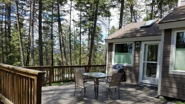 Une terrasse en bois avec une table et des chaises, donnant sur une zone boisée.