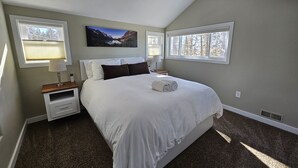 Une chambre à coucher avec un grand lit, deux tables de chevet, une commode, un tableau au mur et deux fenêtres.