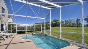 A swimming pool with a covered area, lounge chairs, and a view of a grassy field and trees. - Golf Course View Villa! Just 25 mins to Disney Magic (Davenport)