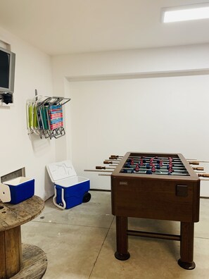 A room with a foosball table, a TV mounted on the wall, and a rack holding various items. - 🏝🏖 Spacious Luxury 4/3 Townhouse  in Gulf Front Gated Community (Pensacola Beach)