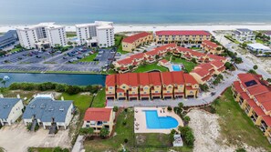 A coastal hotel with multiple buildings, a swimming pool, and a parking lot.