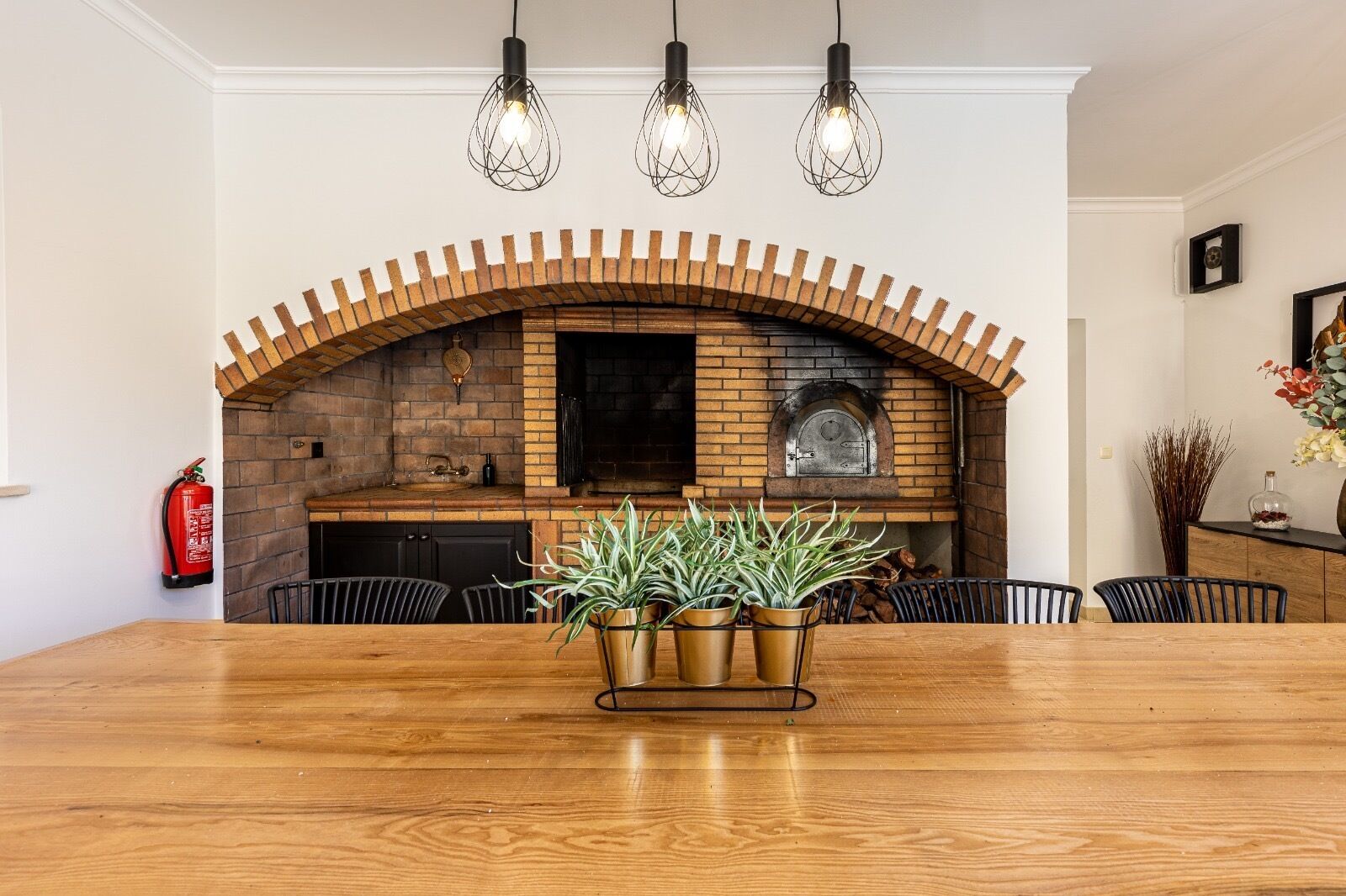 A dining area with a wooden table, chairs, a brick fireplace, and hanging pendant lights.