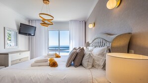 A modern hotel room with a large bed, a flat-screen TV, and a view of the sea through the window. - Luxurious house with sea and mountain views (Arco da calheta)