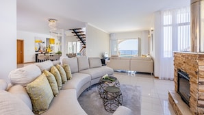 A modern living room with a curved sofa, a fireplace, and a view of the sea. - Luxurious house with sea and mountain views (Arco da calheta)