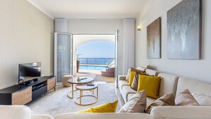 A modern living room with a TV, sofa, and coffee table, leading to a balcony with a view of the sea. - Luxurious house with sea and mountain views (Arco da calheta)