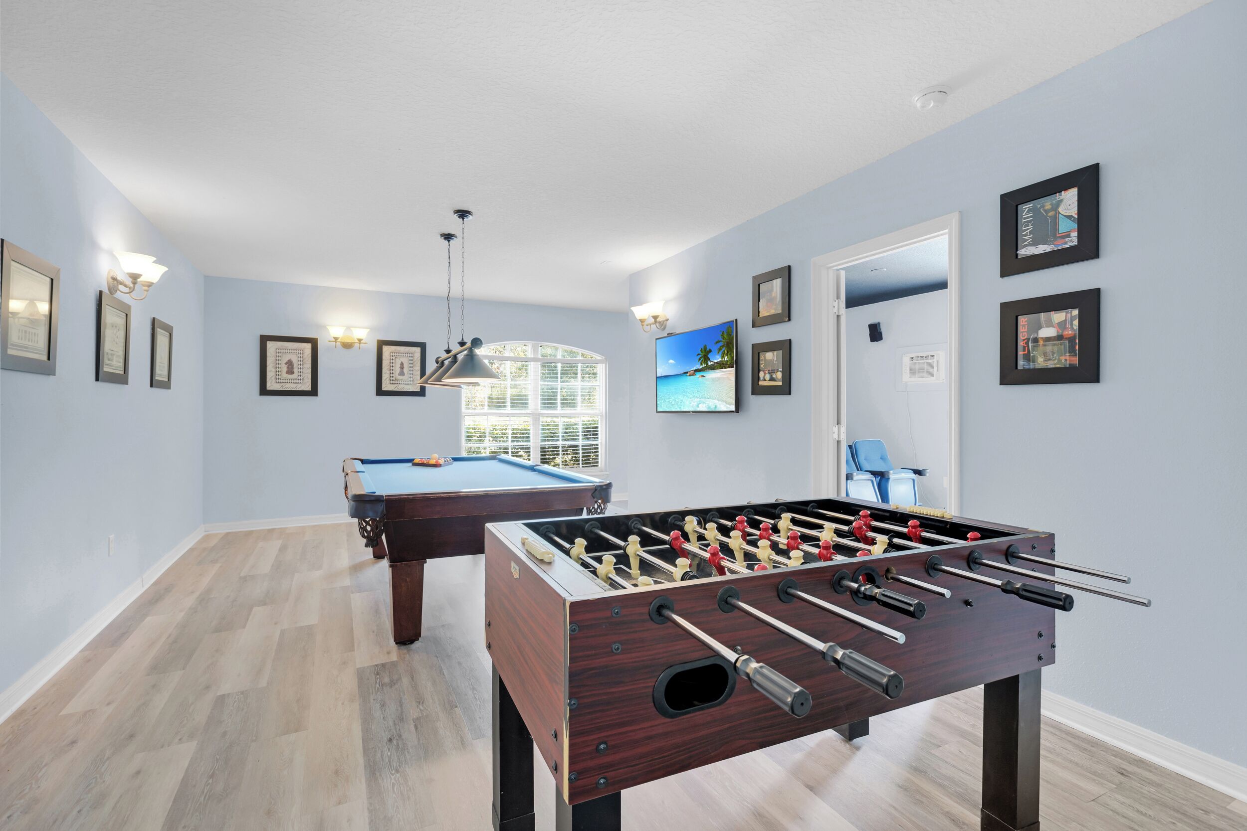 A room with a foosball table, a pool table, and a billiards table.
