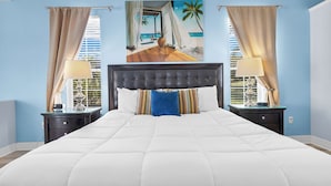 Una camera da letto con un letto grande, due comodini, un quadro raffigurante una spiaggia e tende alle finestre.
