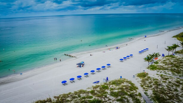 Ein Strand mit klarem türkisblauem Wasser, weißem Sand und blauen Sonnenschirmen.