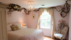 Un dormitorio con una cama grande, una silla, una araña y detalles decorativos florales.