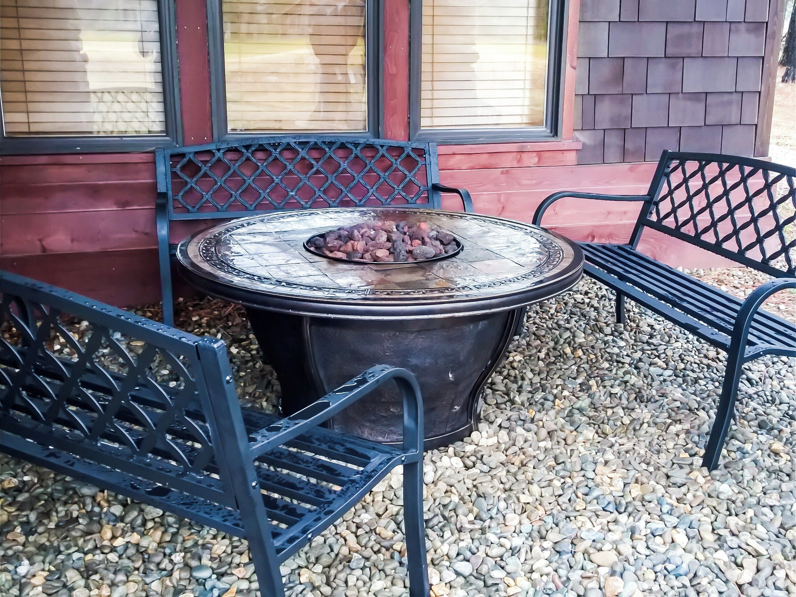 An outdoor seating area with a fire pit table and metal chairs, surrounded by pebbles.