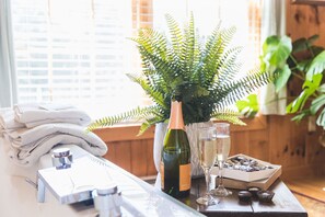 A table with a bottle of wine, glasses, a box of chocolates, and a potted fern. - Rustic Romantic Bayberry Cottage at Autumn Ridge (Lexington)